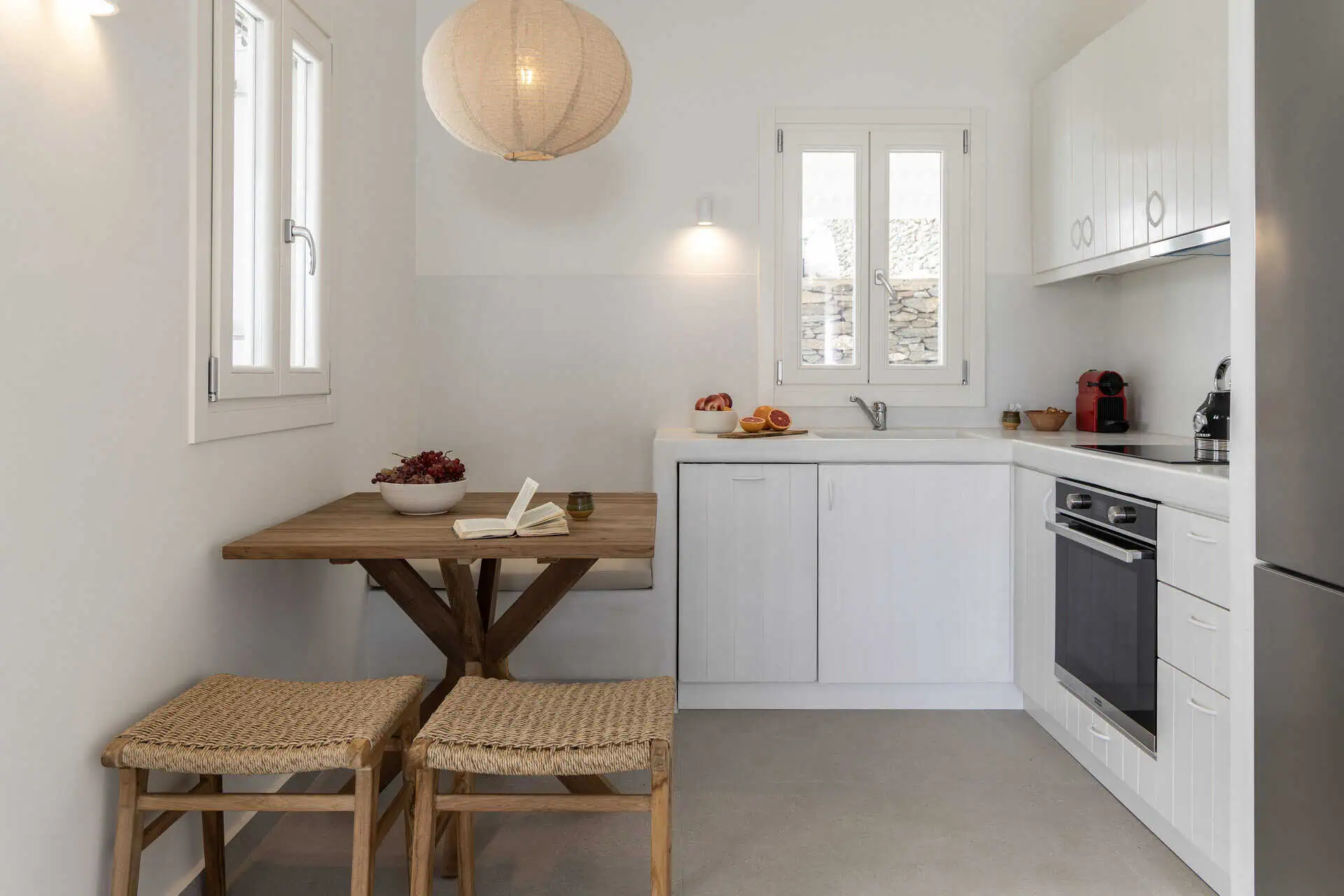 Cozy kitchen with white cabinets, a wooden dining table, and woven chairs in a villa in Aosa, Kythnos.