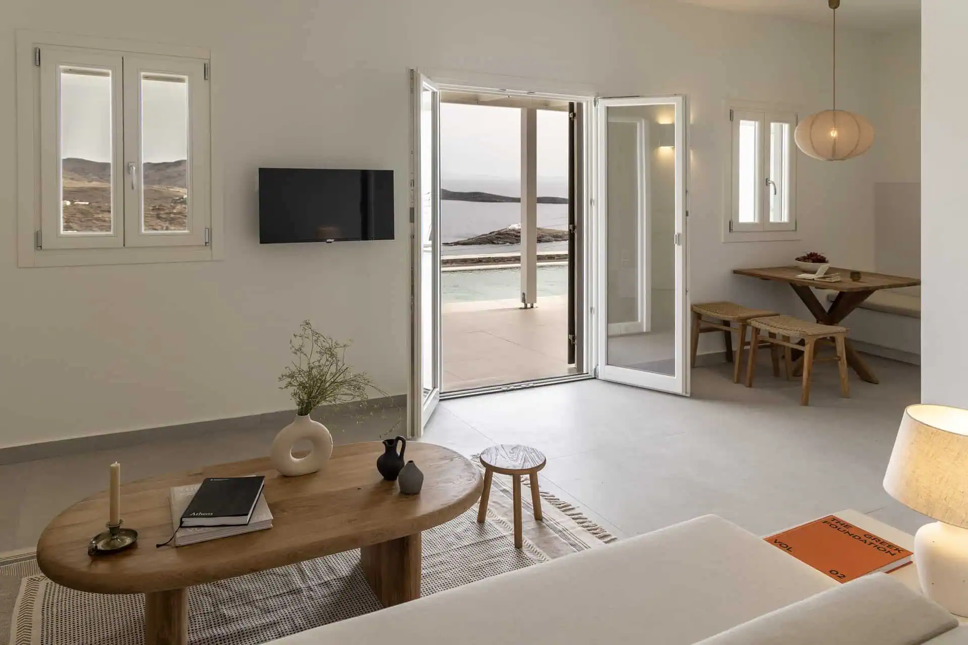 Living room opening to an outdoor pool and sea view, with minimalist furniture in a villa in Aosa, Kythnos.