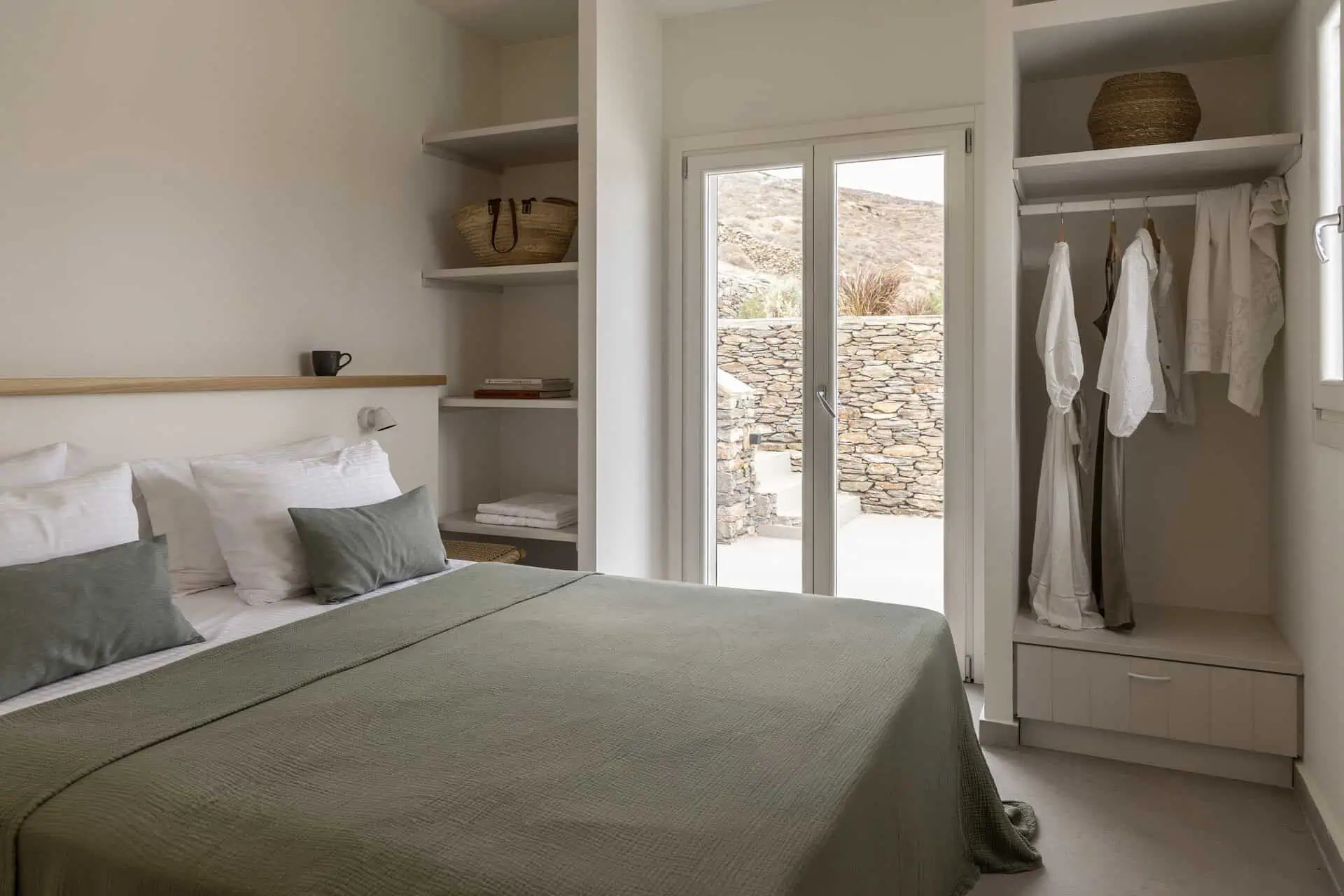 Minimalist bedroom with a double bed, olive-green bedding, and open closet in a villa in Aosa, Kythnos.
