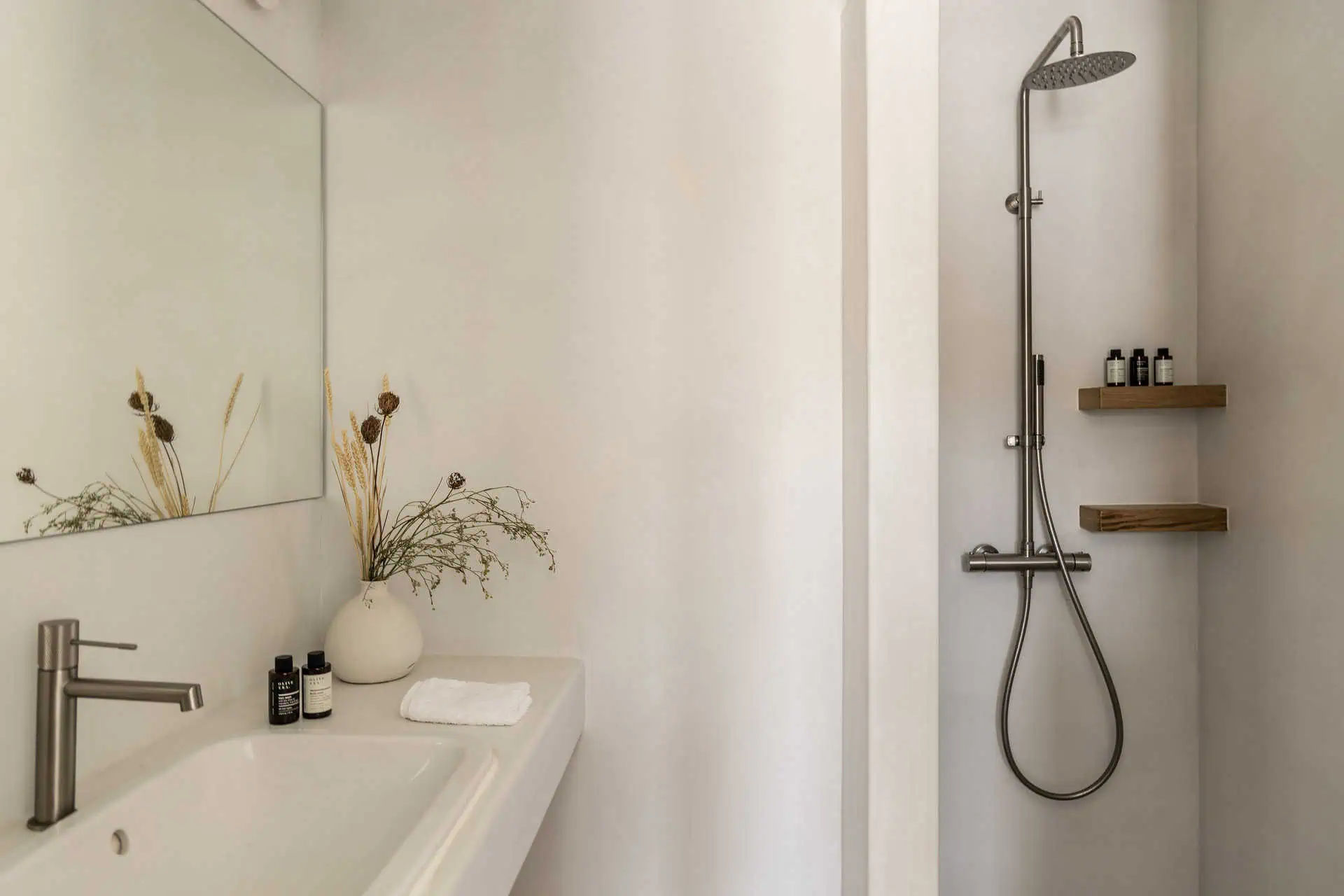 Modern bathroom with a walk-in rain shower, simple white sink, and dried floral arrangement in Aosa, Kythnos.