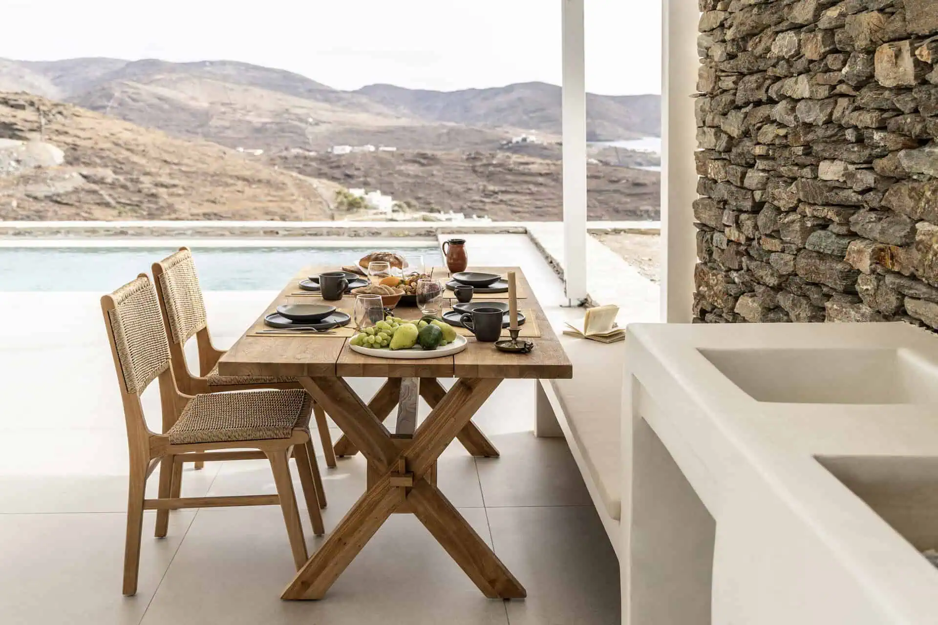 Outdoor dining area showcasing a wooden table and chairs, overlooking a pool and scenic hills in Aosa, Kythnos.