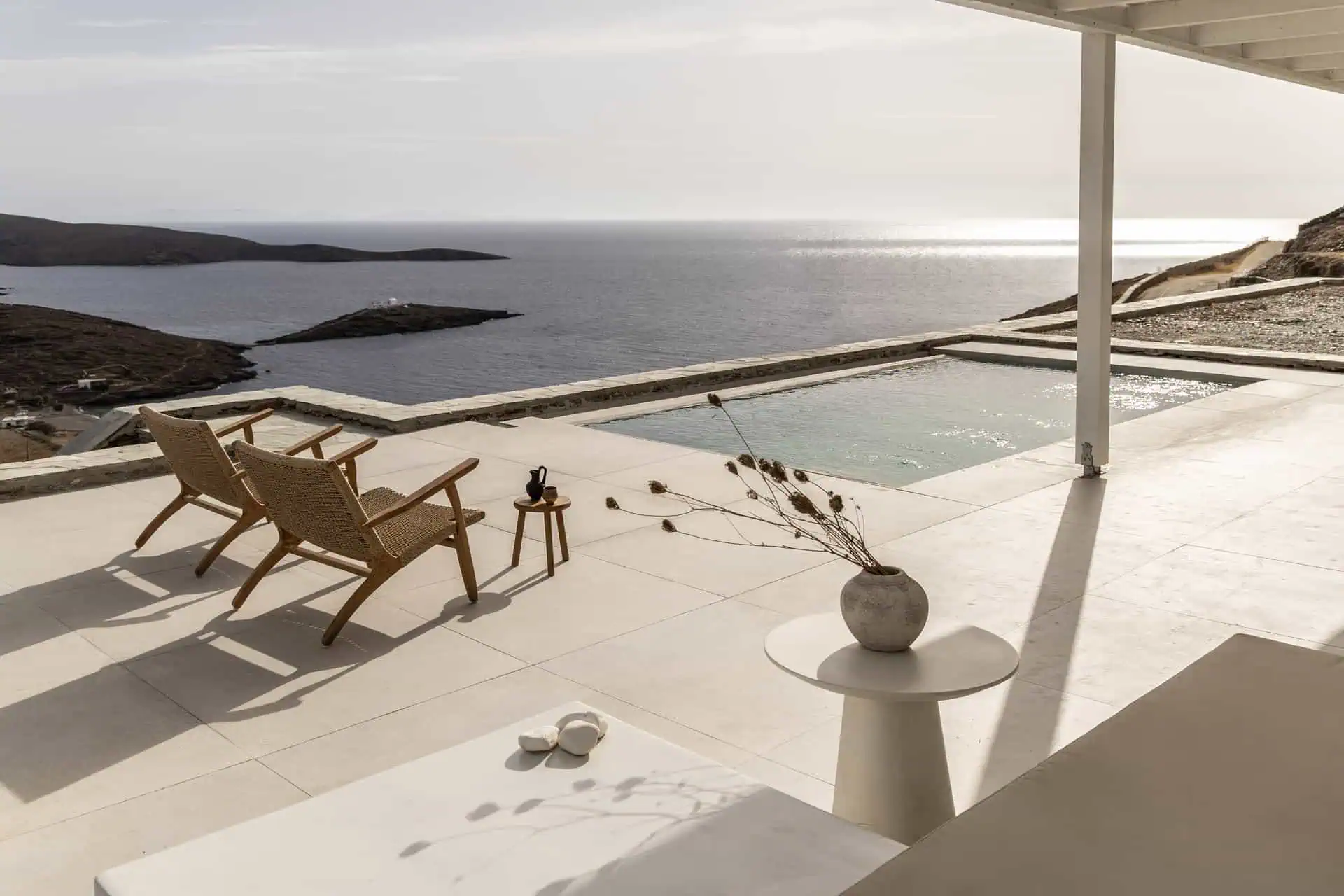 Outdoor patio with two wooden chairs overlooking a serene infinity pool and the Aegean Sea in Aosa, Kythnos.