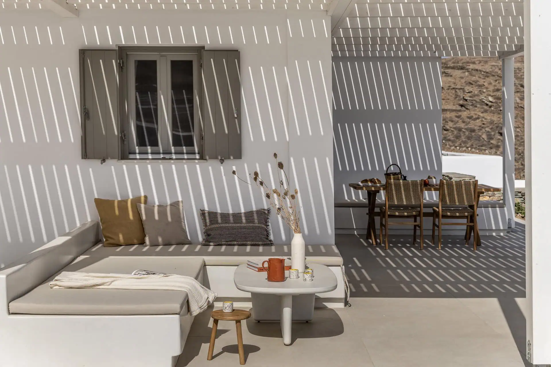 A shaded outdoor patio with a cozy lounge area, a coffee table styled with decor, and a dining space featuring wooden chairs and a table.